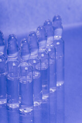 Glass medical ampoule vial for injection. Medicine is liquid sodium chloride with of aqueous solution in ampulla. Close up. Bottles ampule multicolor on background color and water. Human plasma.