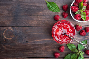 Homemade raspberry jam in a glass jar and fresh raspberries with mint on a wooden rustic background. Copy space