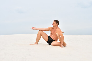 Fototapeta na wymiar Man sitting on sand in yoga pose on the beach