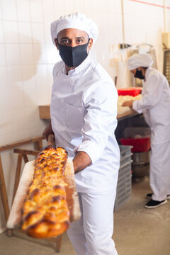 Professional Latin American Baker Taking Freshly Baked Hot Bread Out Of Oven On Wooden Shovel In Small Bakery