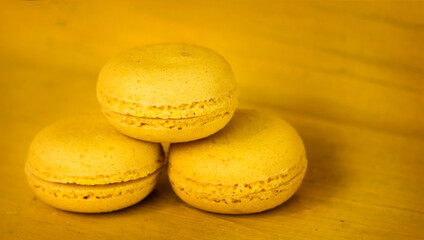 three yellow delicious almond cookies stacked in a pyramid on a yellow wooden background