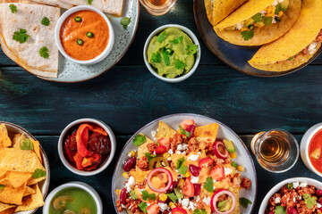 Fototapeta na wymiar Mexican food background. Nachos, tacos, guacamole, tequila, quesadillas, overhead shot on a dark blue wooden table with a place for text