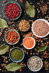 Various legumes, shot from the top on a dark background. Lentils, soybeans, chickpeas, red kidney beans, black-eyed peas and other pulses, a flat lay