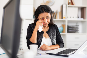 Portrait of frustrated female entrepreneur sitting at office desk with papers and laptop