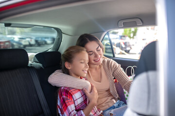 Mom hugging her daughter, sitting cheek to cheek on backseat of car