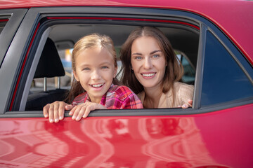 Happy daughter and her mom looking out the window on backseat of car