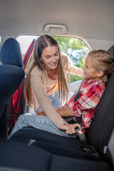 Caring mom fastening her daughter's safety belt on backseat of car
