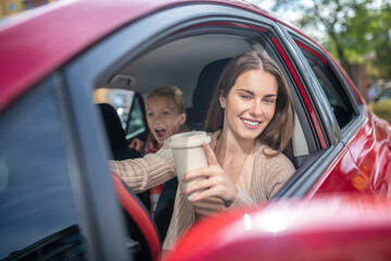 Smiling mom holding coffee cup, driving with her amazed daughter