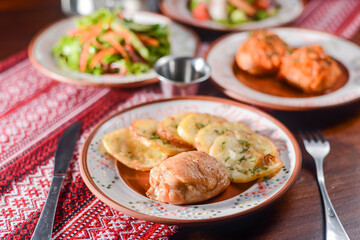 Traditional Ukrainian dishes in ceramic plates - baked potatoes, fried meat, fresh vegetable salad.