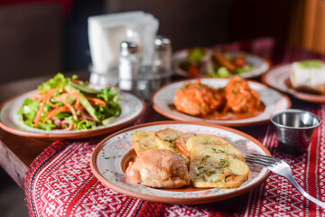 Traditional Ukrainian dishes in ceramic plates - baked potatoes, fried meat, fresh vegetable salad.