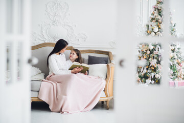 Obraz na płótnie Canvas Two happy girls, mother and daughter siting on a sofa in Christmas decorated room.