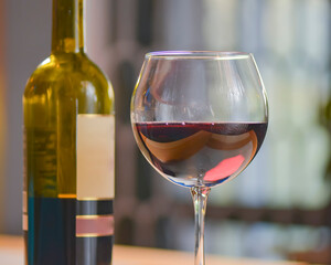 Wine glass and bottle of red wine on a wooden table over blurred background. Restaurant service, eating out concept.