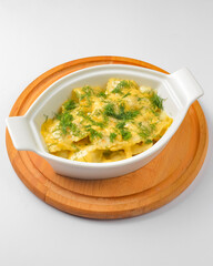 Ravioli dumpling with fresh greenery served in a white pot over white background. Isolated on white.