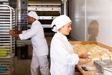 Professional hispanic female baker portioning dough with scraper and weighing pieces