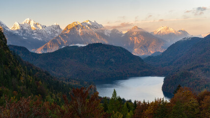 Fototapeta na wymiar Panorama view of lake alpsee in the morning with snow peaks mountains in alpenglow