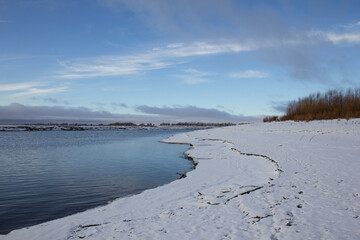 Freezing river. The river bank covered with snow and ice. Cold water under the blue sky.