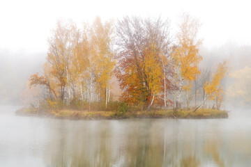 Obraz premium Small island in autumn colors with morning mist, fog