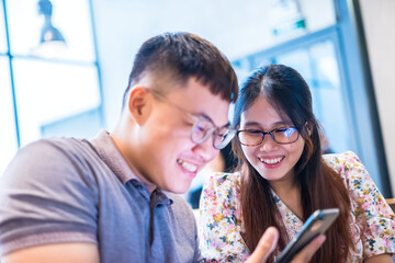 Happy asian couple in coffee shop using smartphone together, smiling young couple embracing while looking at smartphone.