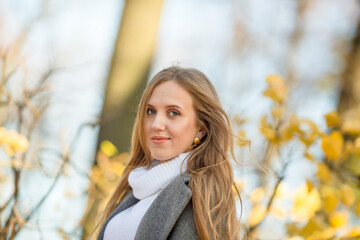 Portrait of a pretty young woman with light brown hair. Beautiful woman in an autumn park against a background of yellow foliage. Fall season.