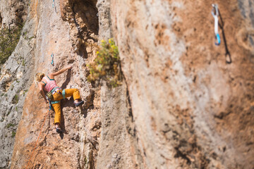 A strong woman climbs a beautiful orange rock.