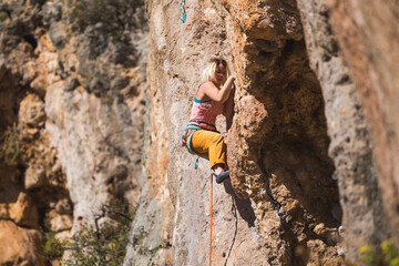Fototapeta premium A strong woman climbs a beautiful orange rock.