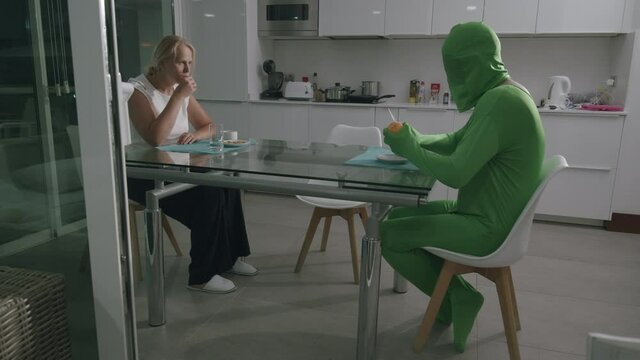 Man wearing a green costume and sitting at the table at home. Communication troubles. He wants nobody to see his emotions