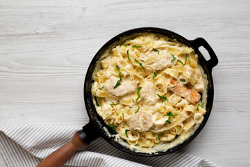 Homemade Chicken Fettuccine Alfredo in a cast-iron pan on a white wooden surface, top view. Flat lay, overhead, from above. Space for text.