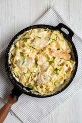 Homemade Chicken Fettuccine Alfredo in a cast-iron pan on a white wooden background, top view. Flat lay, overhead, from above. Close-up.