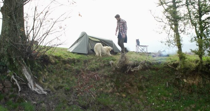Young man with man's best friend. Man with his dog camping near bonfire, in front of tent 
