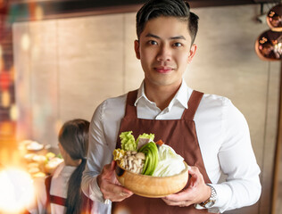 young waiter bring vegetables for hot pot and serving customer  in restaurant