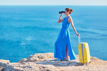 Woman looking in binoculars with sea view. Lady in dress with suitcase. New ground and travel time idea, copy space