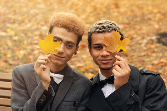 Young Handsome Black Gay Couple In Love Sitting On Bench In Park During Autumn Holding Yellow Leaves (selective Focus). Concept Of Same Sex Love, Equality And LGBT Rights. Black Lives Matter!