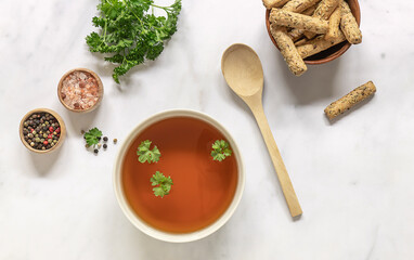 Homemade beef bone broth in a bowl with ingredients. Top view.