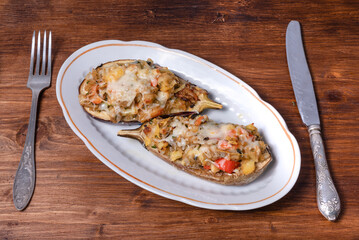 Eggplant baked with vegetables and cheese on an oval plate on a wooden table with cutlery