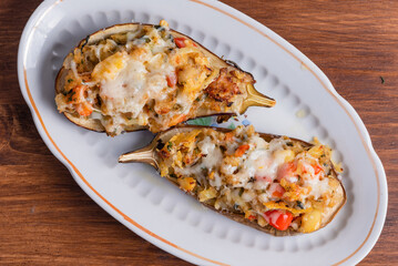 Baked eggplants with vegetables and cheese on an oval plate on a wooden table, top view, close-up