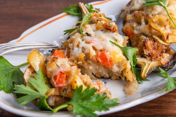 Baked eggplant with vegetables and cheese sprinkled with chopped parsley on an oval plate on a wooden table with a fork and knife, close-up