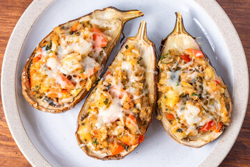 Halves of eggplant baked with vegetables and cheese , karniyarikon a plate on a wooden table, close-up, top view, macro