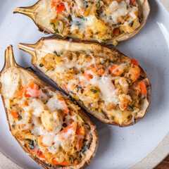 Halves of eggplant baked with vegetables and cheese, karniyarik on a plate on a wooden table, close-up, top view, macro