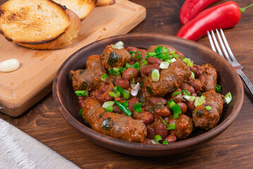 Traditional country Texas cowboy dish, beef sausages with beans in tomato sauce in a rustic clay plate with toast on a wooden table, close-up