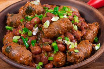 Traditional country Texas cowboy dish, beef sausages with beans, onions in tomato sauce in a rustic clay plate on a wooden table, close-up