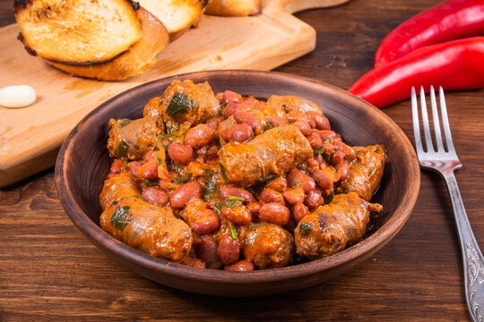 Traditional country Texas cowboy dish, beef sausages with beans in tomato sauce in a rustic clay plate with toast on a wooden table, close-up