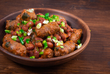 Traditional country Texas cowboy dish, beef sausages with beans, onions in tomato sauce in a rustic clay plate on a wooden table, close-up