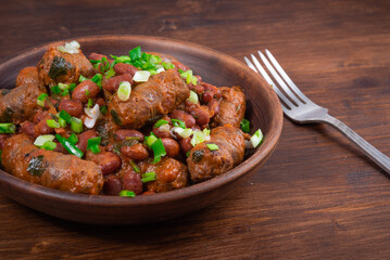 Traditional country Texas cowboy dish, beef sausages with beans, onions in tomato sauce in a rustic clay plate on a wooden table, close-up