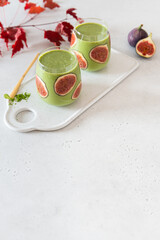 Healthy smoothie with banana and Matcha tea decorated with figs in glasses on a gray backgground. Side view, copy space. Green Matcha tea smoothie recipe, detox, dieting, healthy food, super foods