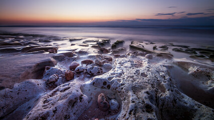 Calm ocean long exposure. Stones in mysterious mist of the sea waves. Concept of nature background. Sunset time on the beach. Sunlight on horizon. Balangan beach, Bali, Indonesia.