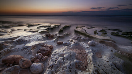 Calm ocean long exposure. Stones in mysterious mist of the sea waves. Concept of nature background. Sunset time on the beach. Sunlight on horizon. Balangan beach, Bali, Indonesia.