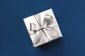 Silver gift box with bow on blue background. Flat lay, top view.