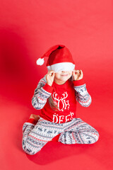 a child in Christmas pajamas sits on his lap and hides under a Santa Claus hat, isolated on a saturation background.
