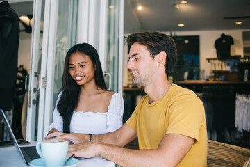 Cheerful couple browsing laptop in cafe