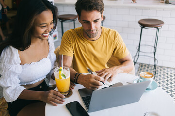 Young couple using laptop and taking notes in cafe